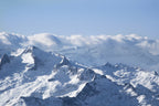 Photographie aérienne des Pyrénées enneigées avec des sommets éclairés par la lumière d’hiver et une mer de nuages au-dessus des montagnes.