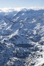 Photographie des Pyrénées en hiver montrant une succession de lacs gelés au cœur des montagnes enneigées, avec une lumière douce sur les reliefs.
