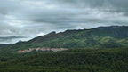 Photographie panoramique d’un village espagnol niché dans les forêts, avec une montagne verdoyante et une lumière traversant le paysage.