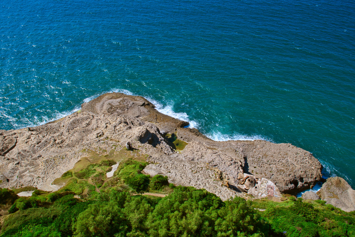 Photographie du littoral basque montrant une falaise rocheuse surplombant l’océan avec une végétation côtière et des reflets de lumière sur les vagues.